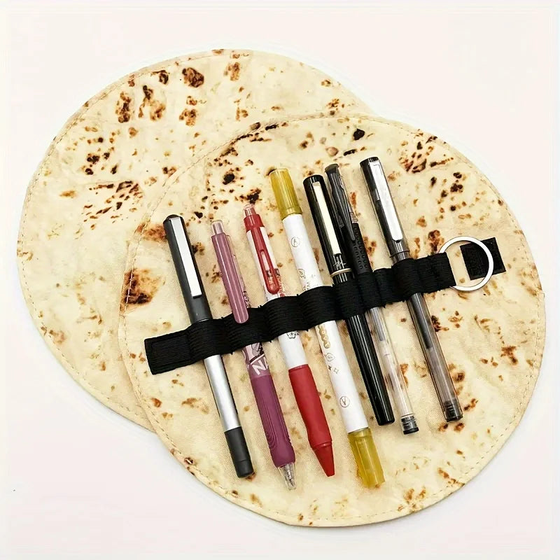 A canvas pencil pouch with a burrito design holds several pens and pencils on a round mat.