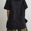 A person wearing a black waterproof outdoor work apron over a dark shirt and olive green shorts.