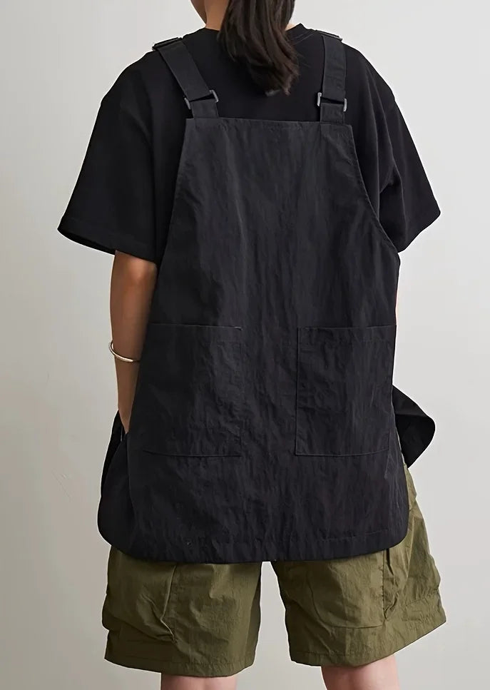 A person wearing a black waterproof outdoor work apron over a dark shirt and olive green shorts.