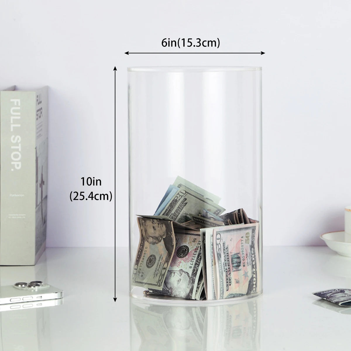 Hucha de acrílico transparente llena de billetes de dólar estadounidense, mostrando sus dimensiones.