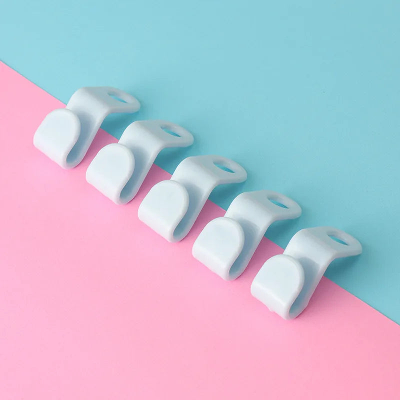 A row of white plastic clothes hanger hooks arranged diagonally on a pink and blue background.