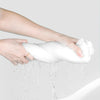 A hand is squeezing a white disposable compressed washcloth, with water dripping from it.