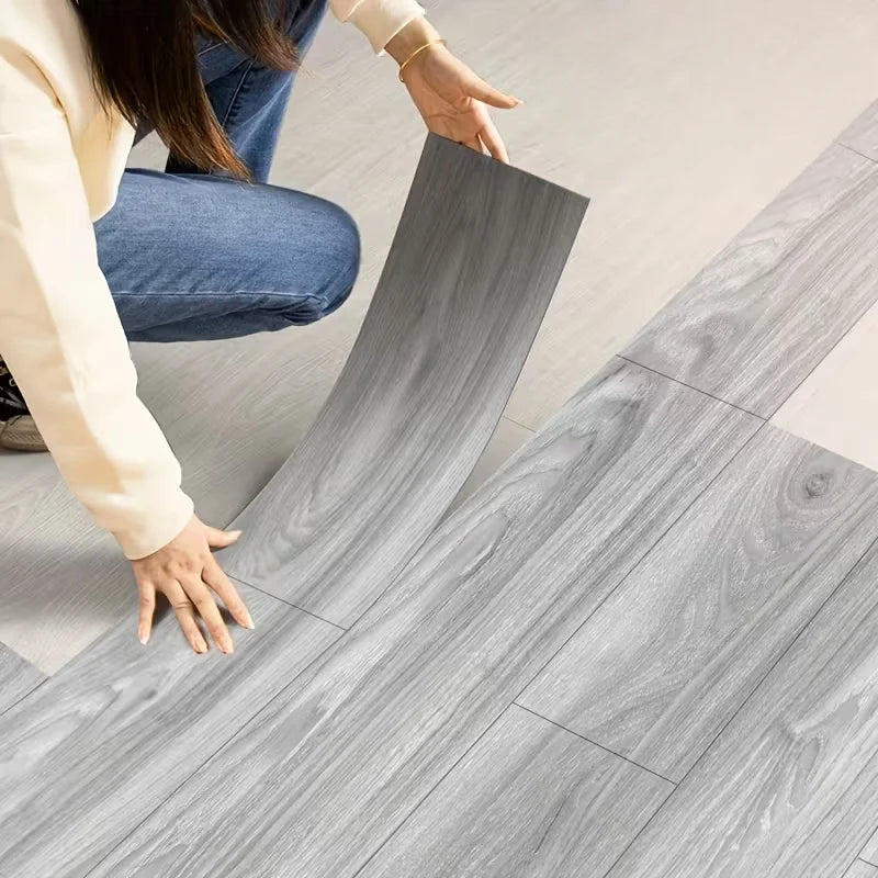 Una persona aplica calcomanías de veta de madera autoadhesivas en un suelo de madera gris claro.