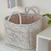 A light floral patterned storage basket with handles sits on a white surface.