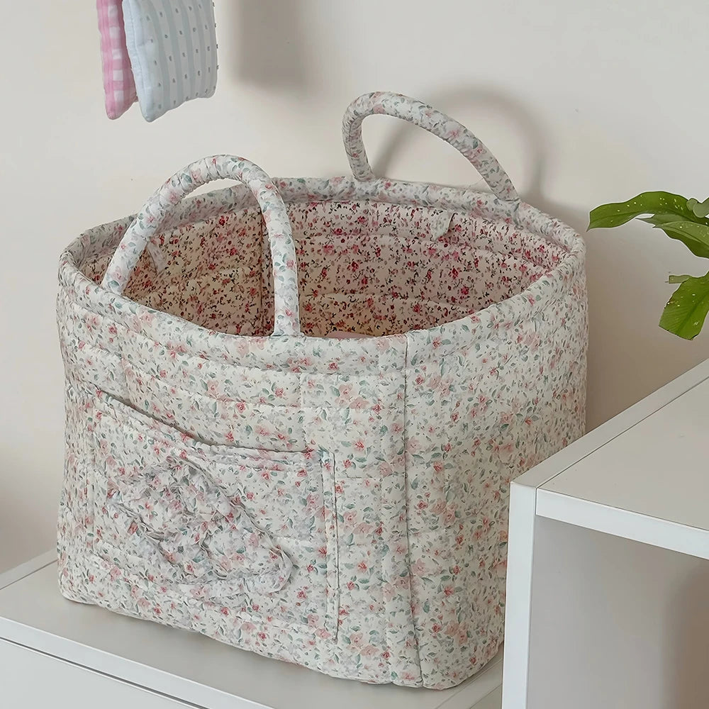 A light floral patterned storage basket with handles sits on a white surface.