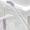 A silver retractable microfiber duster with a fluffy head is suspended from the ceiling in a bright room.