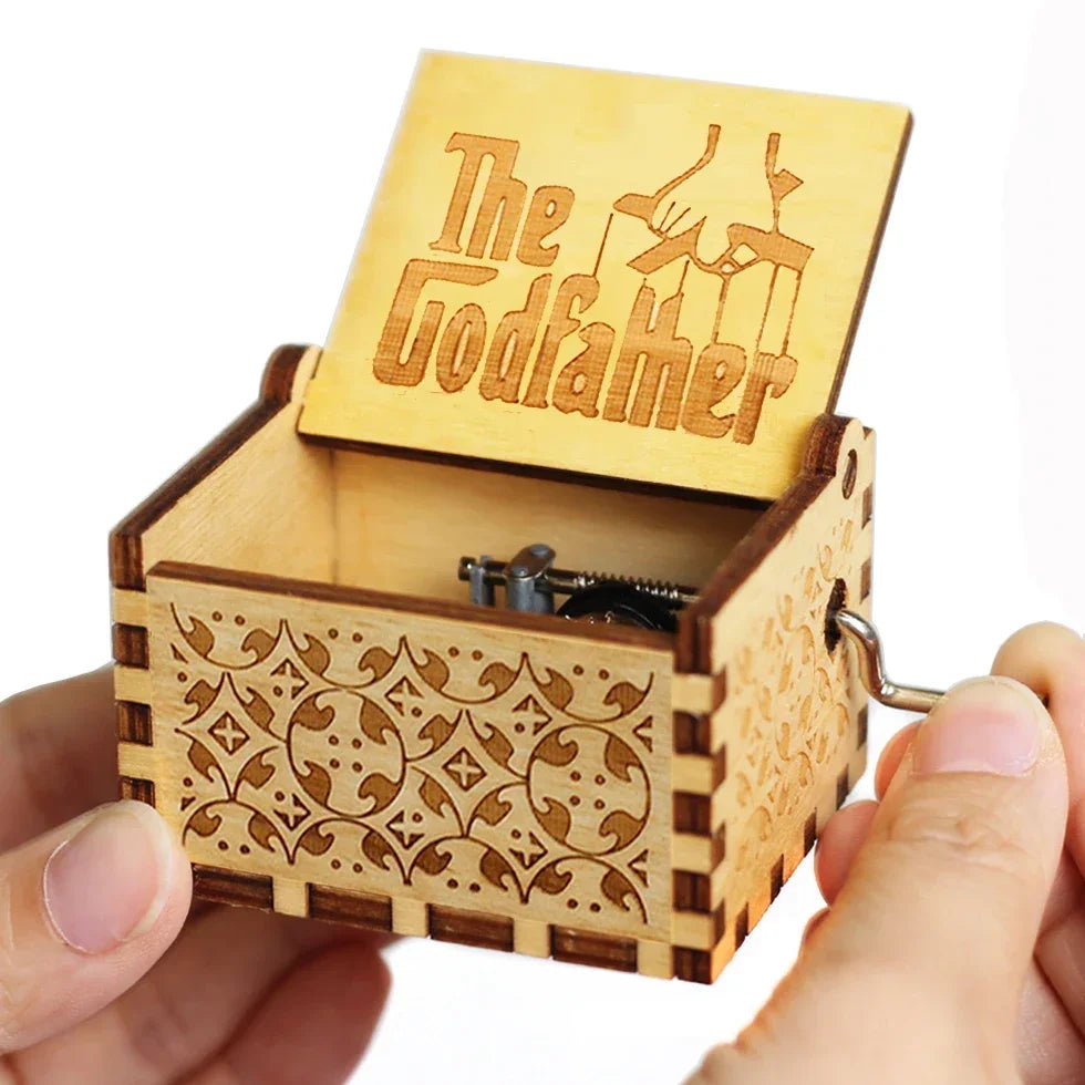 An antique wooden hand crank music box with a lid featuring the name Godfamer is held in a person's hand.