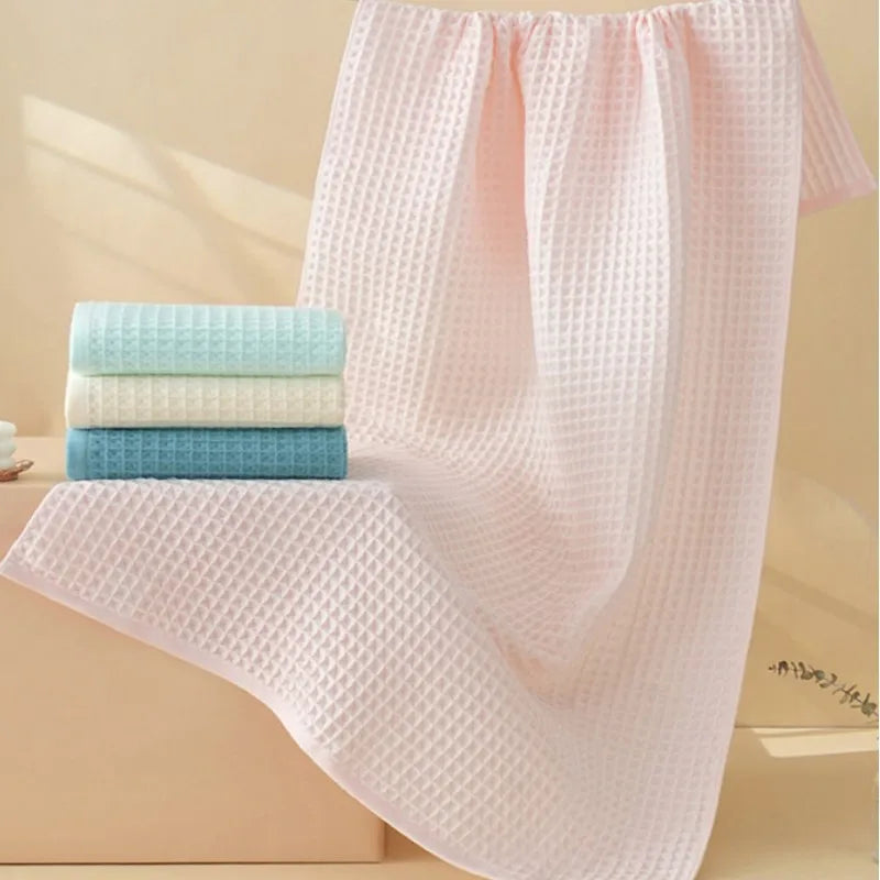 Ein Set aus rosa und hellblauen Waffeltextur-Badetüchern auf einer Holzoberfläche.