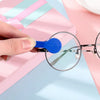 A hand holds a blue cleaning brush for an eyeglasses cleaning set on a pink surface.