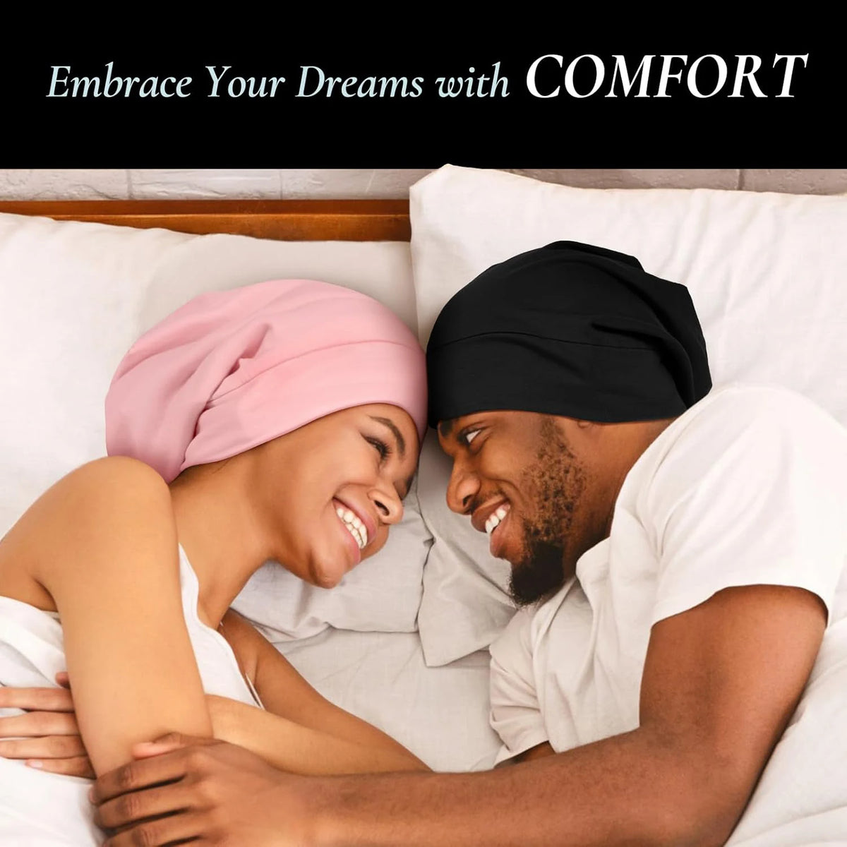 A smiling couple wearing satin sleep bonnets while relaxing in bed.