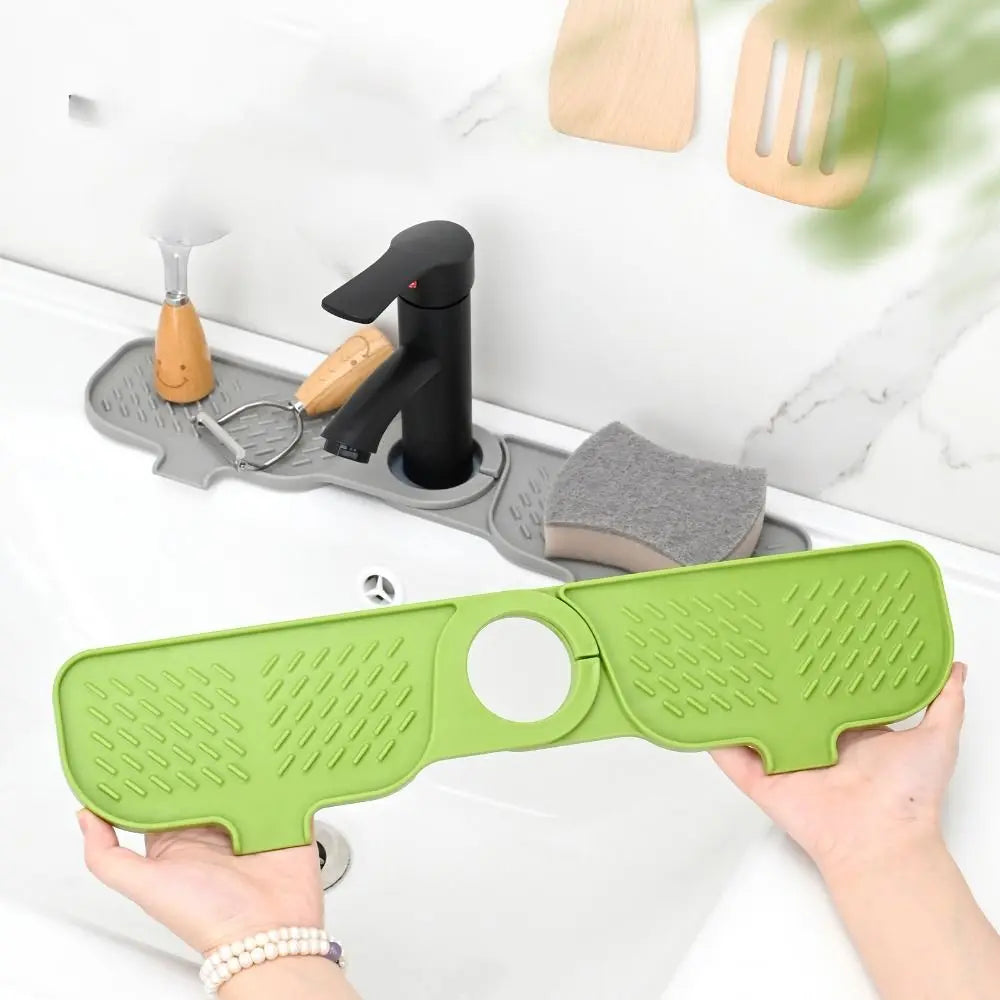 A hand holds a green silicone sink splash guard mat with a hole, next to a faucet and wooden tools.