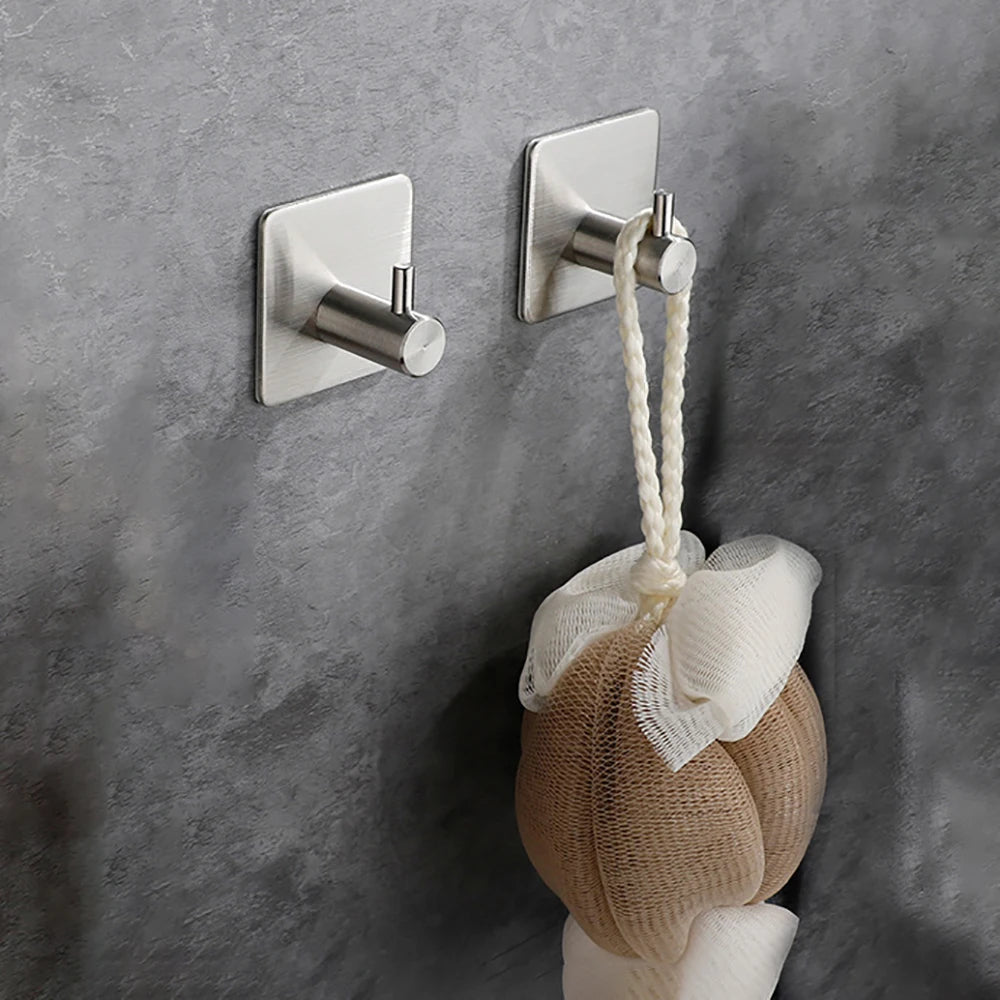 Un toallero adhesivo de acero inoxidable con colgador de cuerda y una toalla beige montado en una pared gris.