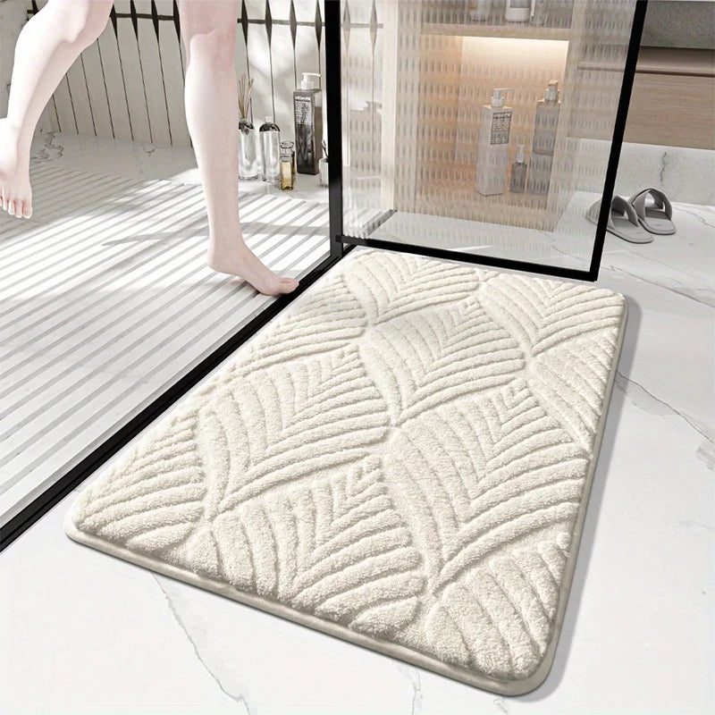 A beige plush non-slip bathroom rug is shown on a white marble floor next to a glass panel.
