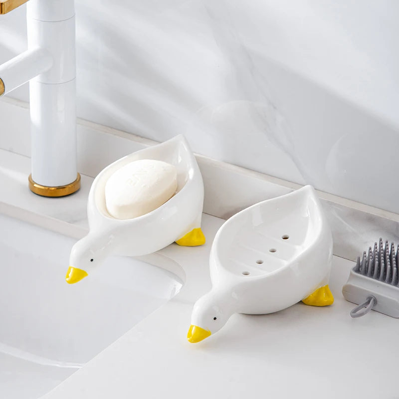 White duck-shaped soap dish with yellow beak sitting on a white bathroom counter.