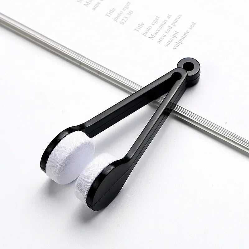 A black silicone cleaning brush set with white microfiber pads is shown resting on a sheet of paper.