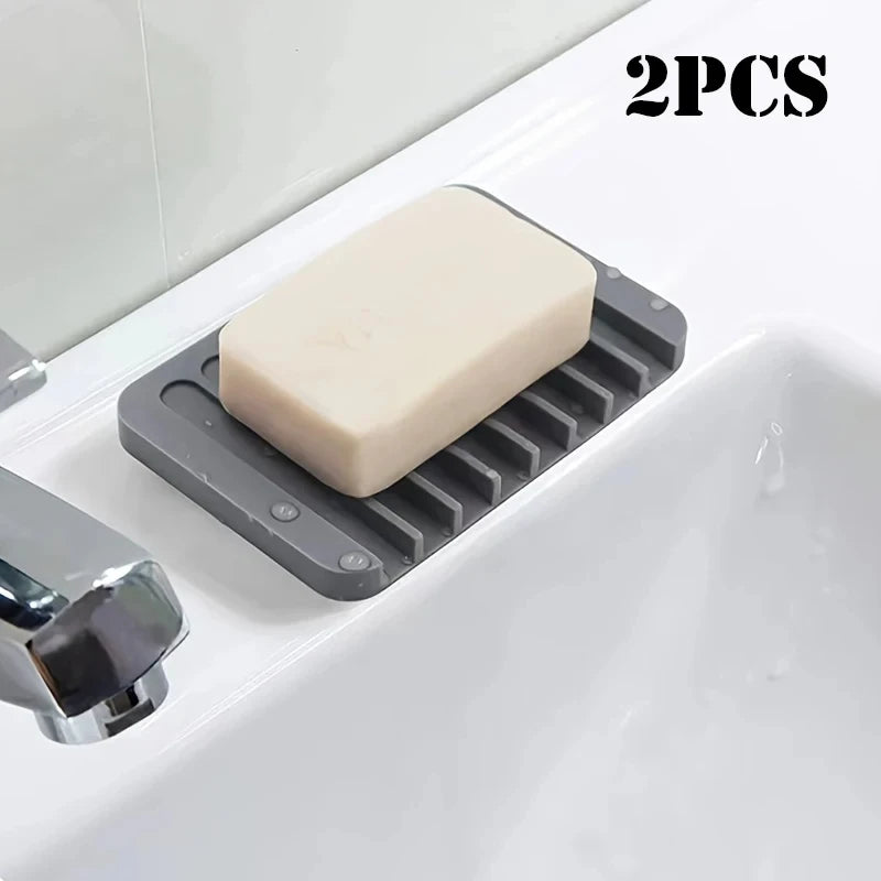 Two silicone soap dishes with anti-slip bases placed in a white bathroom sink.