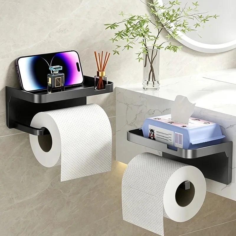 A black no-drill toilet paper holder with a storage shelf displaying a smartphone and decorative items.