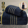 A stack of two dark navy blue bath towels with gold trim, shown next to a woman wearing a matching navy dress.