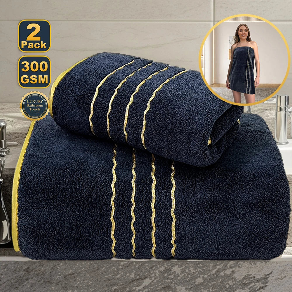 A stack of two dark navy blue bath towels with gold trim, shown next to a woman wearing a matching navy dress.