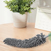 A gray fluffy fiber dust duster is shown next to a potted plant on a wooden surface.