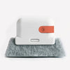A white cleaning brush with an orange section rests on a gray felt surface.