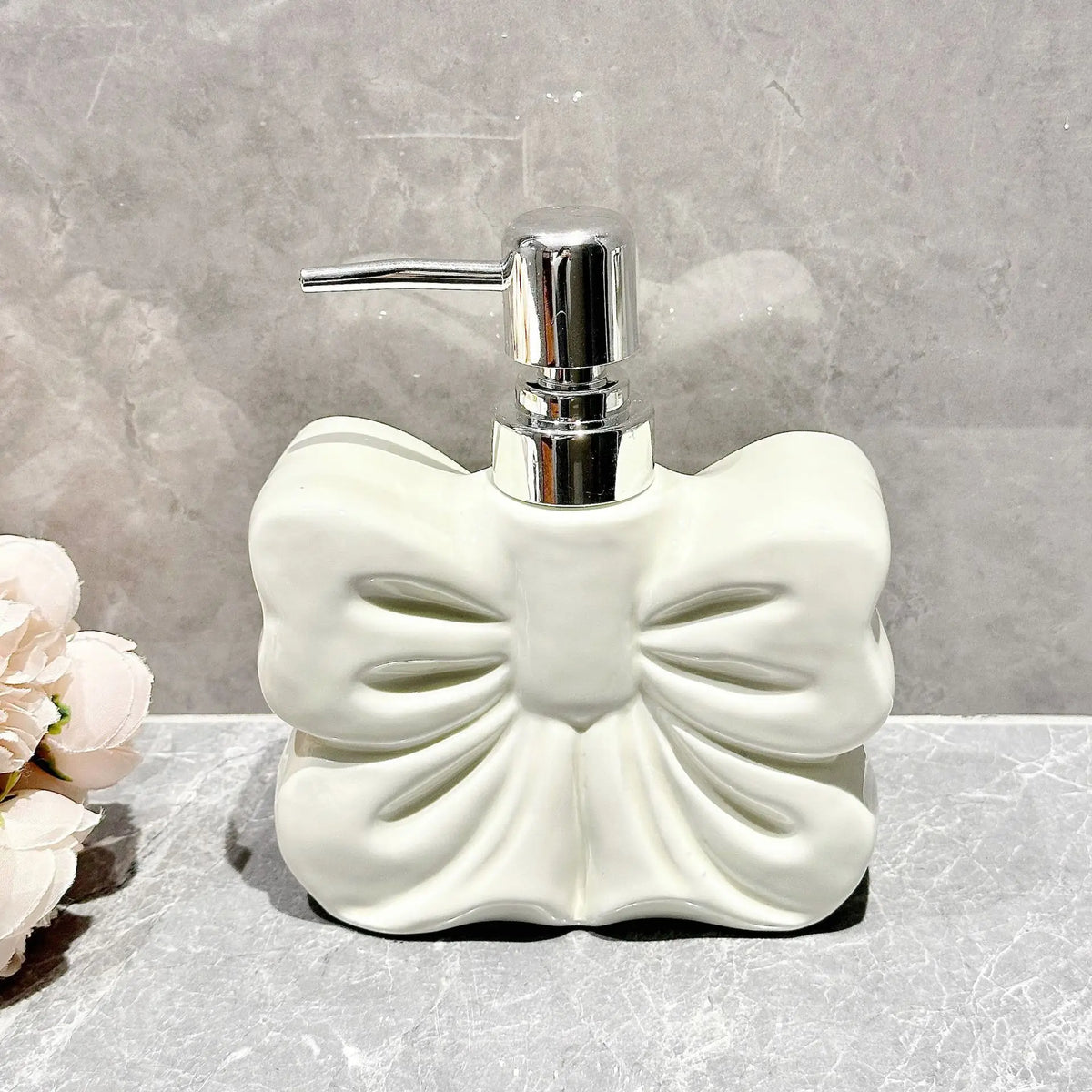 A white ceramic pump dispenser bottle with a bowknot design and a silver pump top.