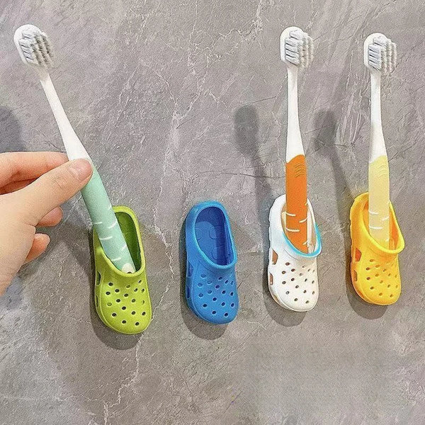 A hand holds a white toothbrush and places it into a colorful adhesive wall mount holder for slippers.