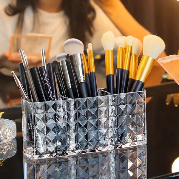 Clear acrylic makeup brush holder with three compartments filled with various makeup brushes