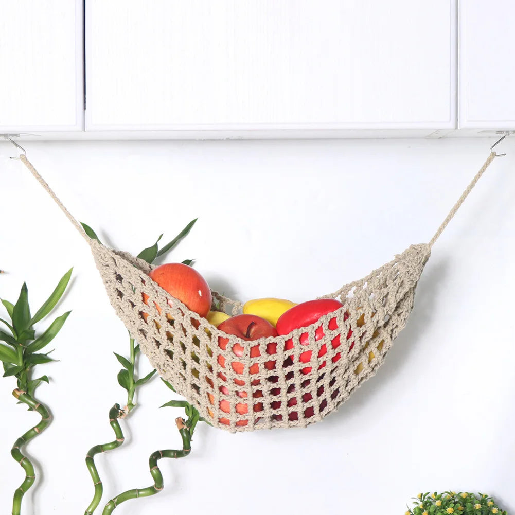 A macrame hanging fruit hammock filled with various colorful fruits is suspended against a white background.