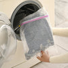 A hand is placing a mesh laundry bag with a pink strap into the drum of a white washing machine.
