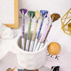A collection of natural amethyst crystal pens in various colors are displayed in a white ceramic cup.