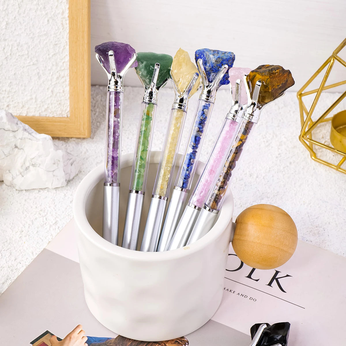 A collection of natural amethyst crystal pens in various colors are displayed in a white ceramic cup.