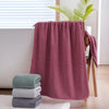 A stack of soft pink towels is displayed next to a wooden hanger and a window.