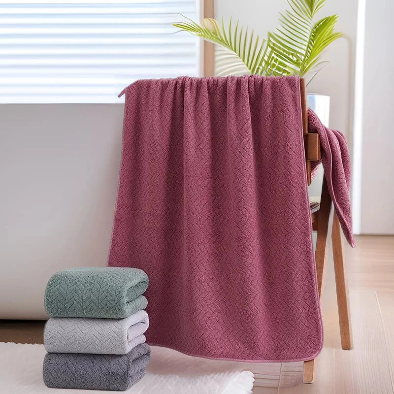A stack of soft pink towels is displayed next to a wooden hanger and a window.