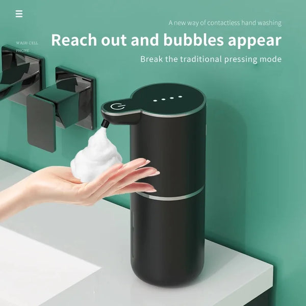 A hand is interacting with a black automatic rechargeable soap dispenser that releases bubbles.