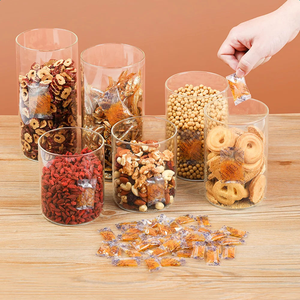 Various dried food ingredients like herbs nuts and fruit pieces are displayed in glass jars on a wooden surface.