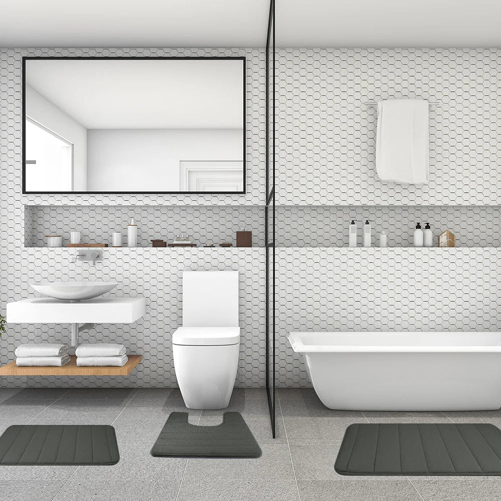 Ein modernes weißes Badezimmer mit Toilette, Waschbereich und Badewanne mit drei dunkelgrauen Memory-Schaum-Matten.