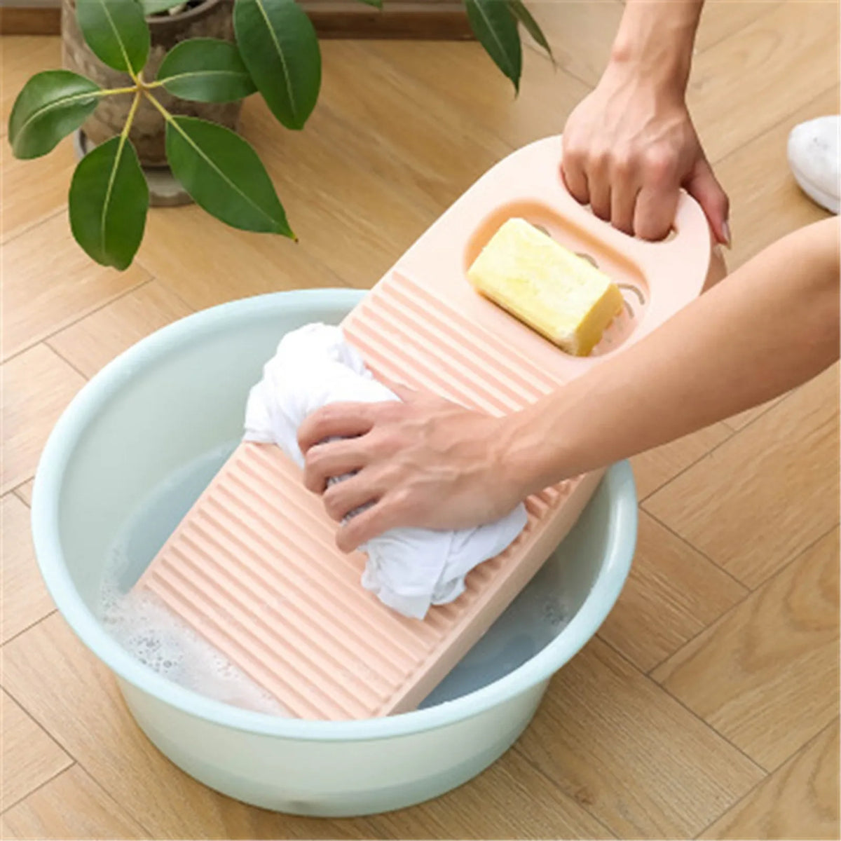 A hand is placing a yellow bar of soap onto a thickened washboard floating in a basin of soapy water.