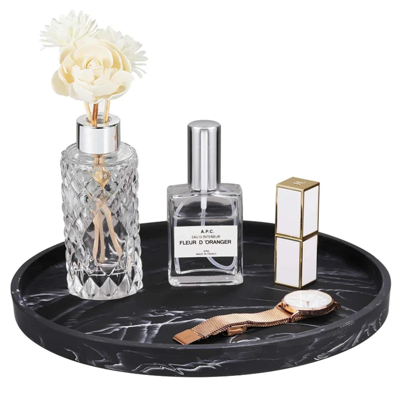 A glass perfume bottle and a gold watch are displayed on a black marble tray.