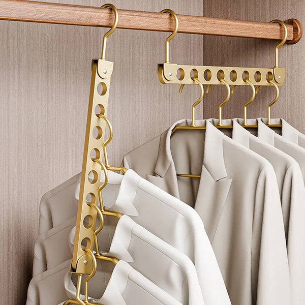 A close-up of a wooden clothing rack with gold-toned hangers holding light beige and white garments.