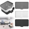 A set of silicone draining soap tray organizers in gray, white, and black are shown with a hand placing a white soap bar on o