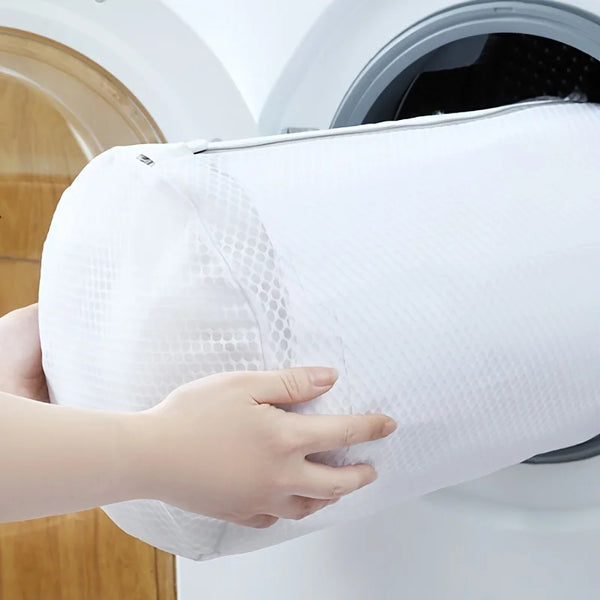 A hand holds a white durable mesh shoe cleaning bag near a washing machine drum.