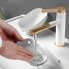 A hand is pouring water into a leaf-shaped bathroom soap dish drainer with a gold and white faucet.