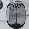 Black foldable mesh laundry basket organizer with two compartments placed next to a white washing machine.
