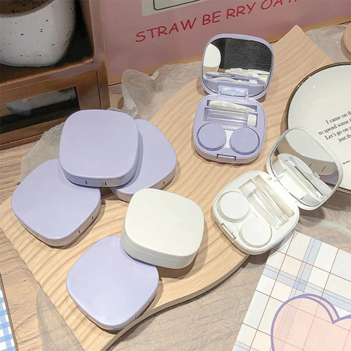 Eine Sammlung von lila und weißen Macaroon-Kontaktlinsen-Aufbewahrungsboxen und eine klare Aufbewahrungsbox werden auf einer 