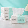 A display of packaged disposable cotton face towels in light green and white on a white surface.