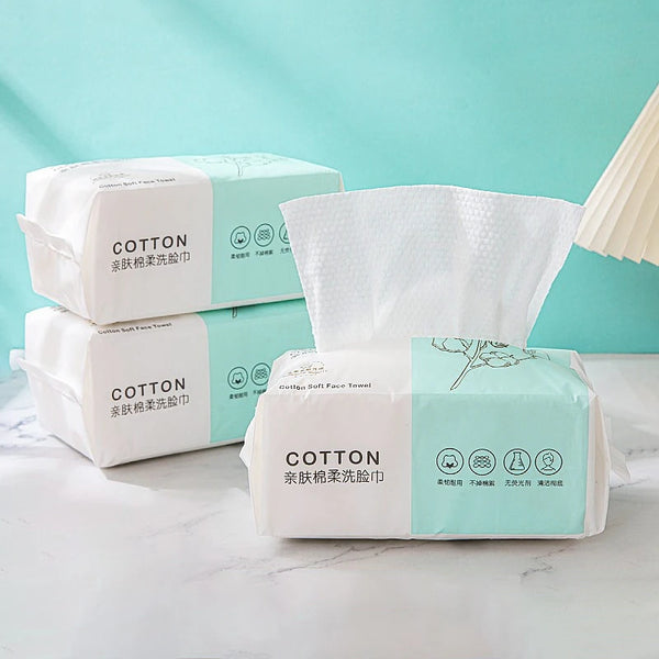 A display of packaged disposable cotton face towels in light green and white on a white surface.