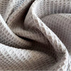 A close-up of a soft, beige waffle weave towel fabric being folded and draped.