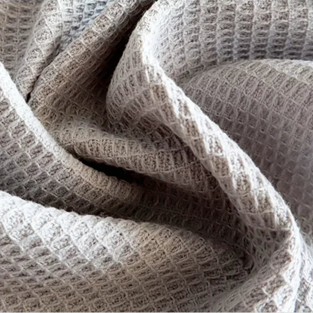 A close-up of a soft, beige waffle weave towel fabric being folded and draped.