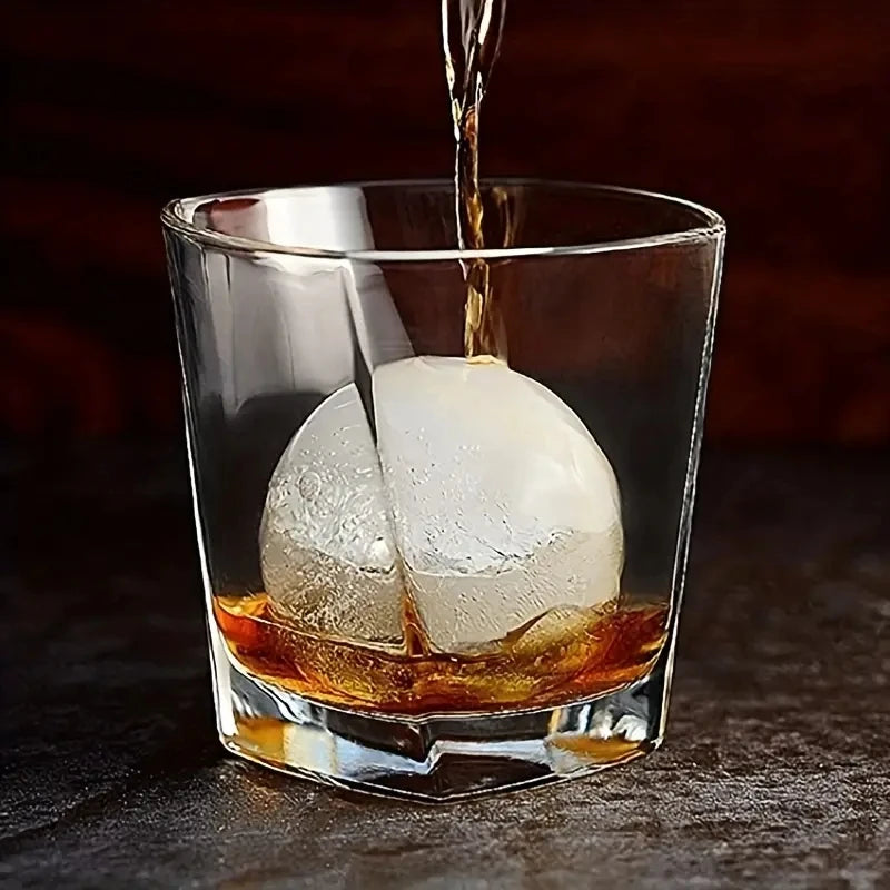 A glass filled with amber liquid and a large ice cube being dropped into the drink.